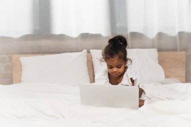 happy african american toddler kid using laptop in bedroom clipart
