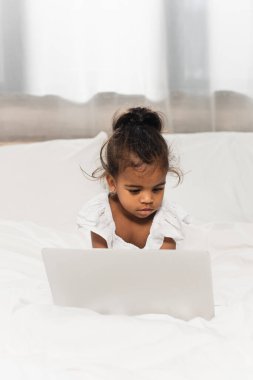 african american toddler girl using laptop in bedroom clipart