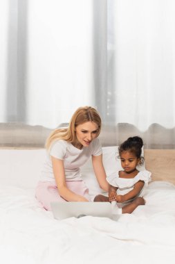 Mutlu anne ve evlat edinilmiş Afrikalı Amerikalı çocuk yatak odasında dizüstü bilgisayardan film izliyor. 