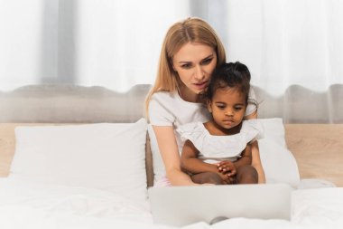 mother and adopted african american kid watching movie on laptop in bedroom  clipart