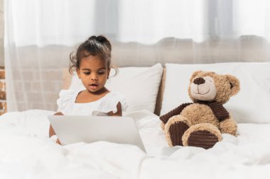 amazed african american child watching movie on laptop near soft toy  clipart