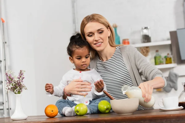 Cheerful Woman Pouring Milk Bowl Holding Adopted African American Daughter — Stock Photo, Image