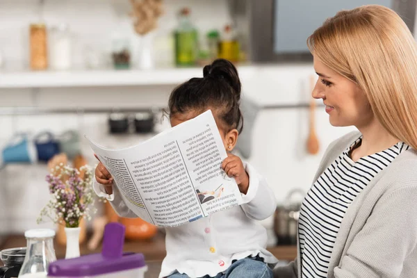 Alegre Madre Mirando Adoptado Africano Americano Niño Con Periódico —  Fotos de Stock