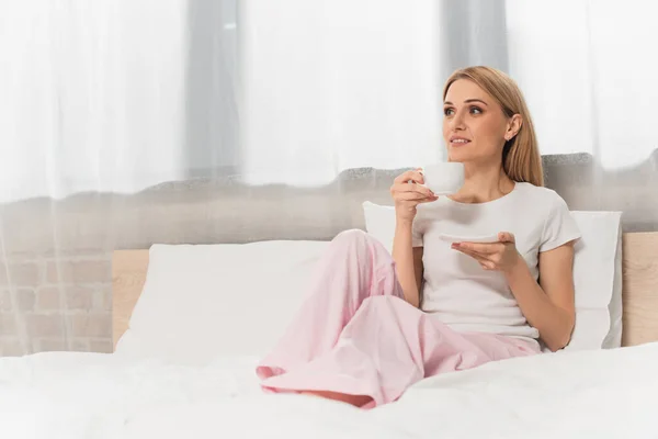 ベッドルームでコーヒーを飲みながら笑顔のブロンドの女性 — ストック写真