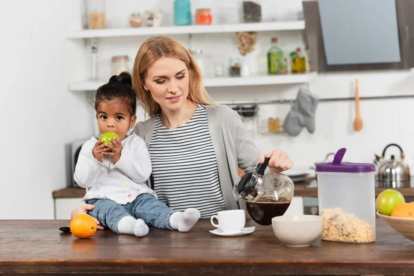 Mujer Verter Café Taza Cerca Adoptado Afroamericano Niño Comiendo Manzana —  Fotos de Stock