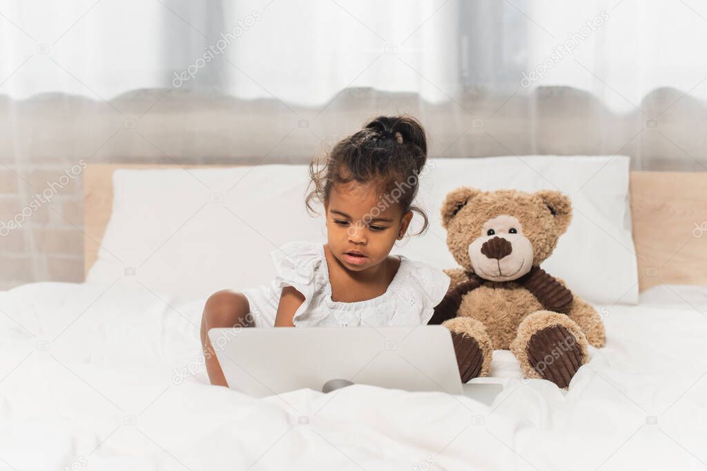 african american kid watching movie on laptop near soft toy 