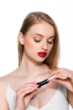 Kırmızı dudaklı güzel bir kadın beyaz ruj tüpüne bakıyor.
