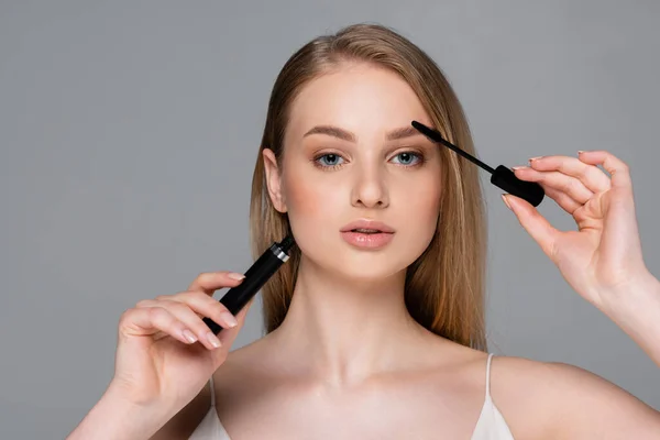 Mujer Joven Sosteniendo Tubo Cepillo Mientras Aplica Rímel Aislado Gris —  Fotos de Stock
