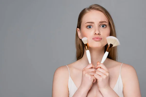 Mujer Joven Sosteniendo Cepillos Cosméticos Cerca Cara Aislada Gris — Foto de Stock