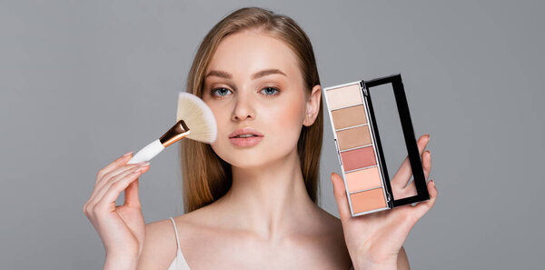 young woman holding cosmetic brush and blush palette isolated on grey, banner