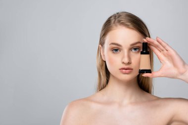 Mavi gözlü güzel bir kadın. Elinde tüp var. Yüz temeli gri renkte. 