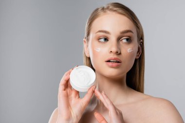 Güzel bir kadın, mavi gözlü, elinde krema kabı olan gri renkli bir kadın.