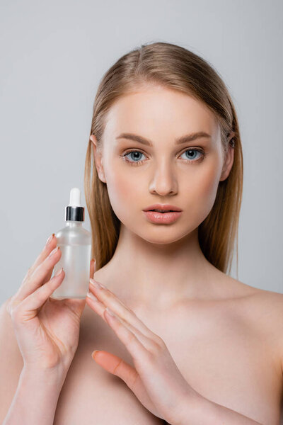 красивая женщина с голыми плечами, держа бутылку с сывороткой, изолированной на сером
