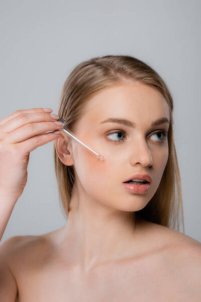 красивая женщина с голыми плечами, применяющая витамин С сыворотку с пипеткой, изолированной на сером