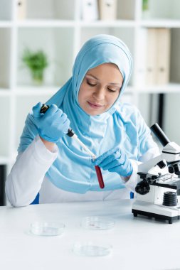 Mikroskop yakınında elektronik pipet ve kan örneğiyle çalışan Müslüman bilim adamı 