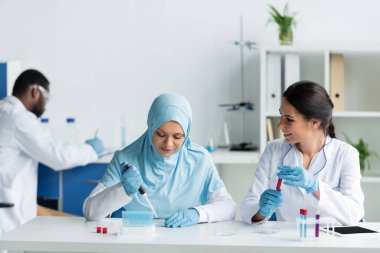 Arap meslektaşının yanında laboratuarda kan örneği tutan gülümseyen bir bilim adamı. 