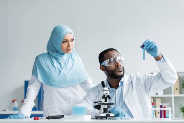 Lateks eldivenli ırklar arası bilim adamları laboratuvarda mikroskop yakınında örneklere bakıyorlar. 