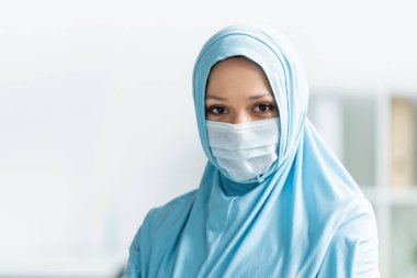 Tıbbi maskeli ve tesettürlü Arap doktor kameraya bakıyor 