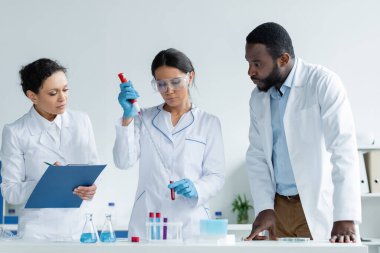 Beyaz önlüklü ırklar arası bilim adamları test tüpleri ve panolarla çalışıyorlar. 