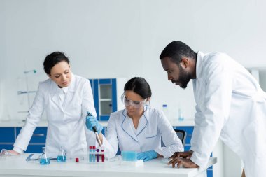 Laboratuvardaki odaklanmış meslektaşlarının yanında pipet ve test tüpleriyle çalışan bilim adamı 