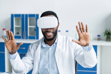 Gülümseyen Afrikalı Amerikalı doktor klinikte sanal gerçeklik kulaklığı takıyor. 