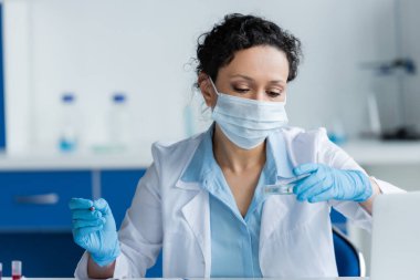 Tıbbi maskeli Afrikalı Amerikalı bilim adamı laboratuarın yanında petri kabı ve kalem tutuyor. 