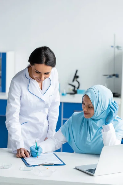 Smiling Arabian Scientist Writing Clipboard Laptop Colleague Petri Dishes — Foto de Stock