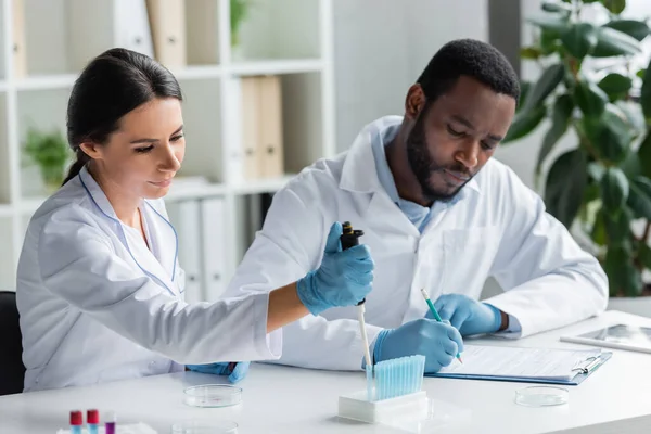 Scientist Holding Electronic Pipette Test Tubes Blurred African American Colleague — Stock Fotó