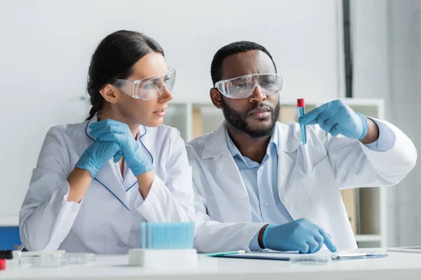 アフリカ系アメリカ人の科学者は ラテックス手袋の同僚の近くに試験管を保持安全ゴーグル — ストック写真
