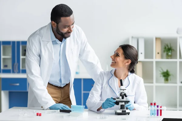 Cientista Sorrindo Para Colega Afro Americano Perto Microscópio Tubos Ensaio — Fotografia de Stock
