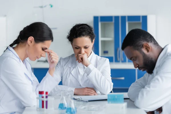 Erschöpfter Wissenschaftler Sitzt Neben Reagenzgläsern Und Klemmbrett — Stockfoto