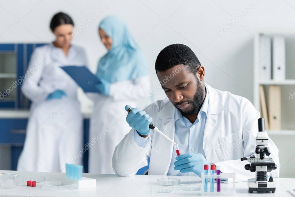 African american scientist researching samples in test tubes near blurred colleagues in lab