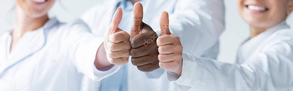 Cropped view of blurred multiethnic doctors showing thumbs up, banner 