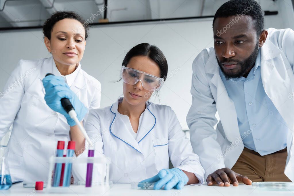 African american scientists looking at colleague making experiment in laboratory 