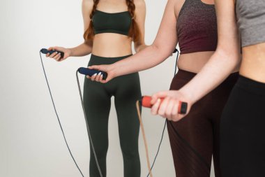 Gri üzerinde izole edilmiş atlama ipleri tutan pozitif kadın sporcular görülüyor. 