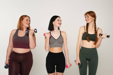 Spor kadınları dambıllarla antrenman yapıyor ve gri renkli çilli arkadaşlara bakıyor. 