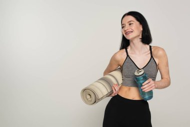 Vitiligo 'lu gülümseyen sporcu kadın spor minderi ve spor şişesini gri renkte tutuyor. 