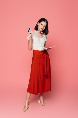 Vitiligo 'su olan genç bir kadın pembe arka planda dijital tablet ve kredi kartı tutuyor. 