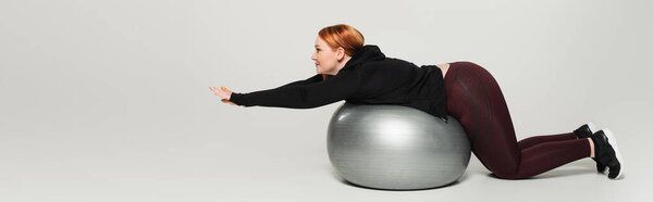 Вид сбоку плюс размер женщины, тренирующейся на фитнес-мяче на сером фоне, баннер 