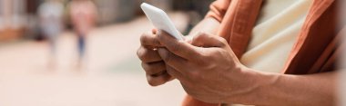 Afro-Amerikan bir adamın açık havada cep telefonuyla mesajlaşmasının kısmi görüntüsü.