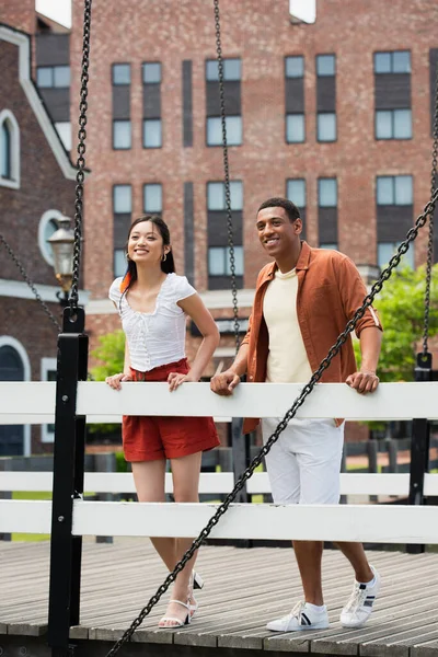 Sorrindo Casal Interracial Olhando Para Longe Enquanto Estava Ponte Cidade — Fotografia de Stock