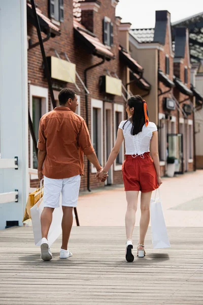 Visão Traseira Casal Interracial Shorts Andando Com Compras Cidade — Fotografia de Stock