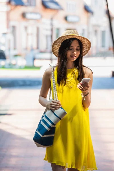 年轻的亚洲女人 穿着黄色的太阳衣 戴着草帽 在户外用智能手机 — 图库照片