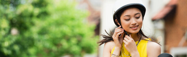 young asian woman fastening helmet outdoors, banner