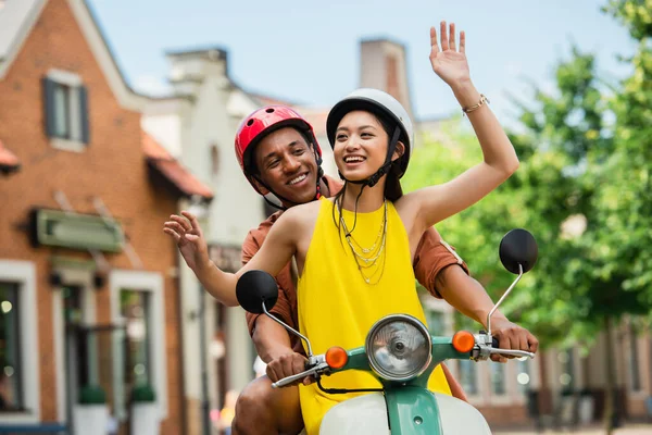 Feliz Asiático Mujer Saludando Mano Mientras Cabalgando Scooter Con Africano — Foto de Stock