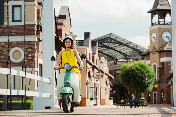 若いですアジアの女性で黄色のサンドレスとヘルメットの乗馬スクーターで街の通り — ストック写真