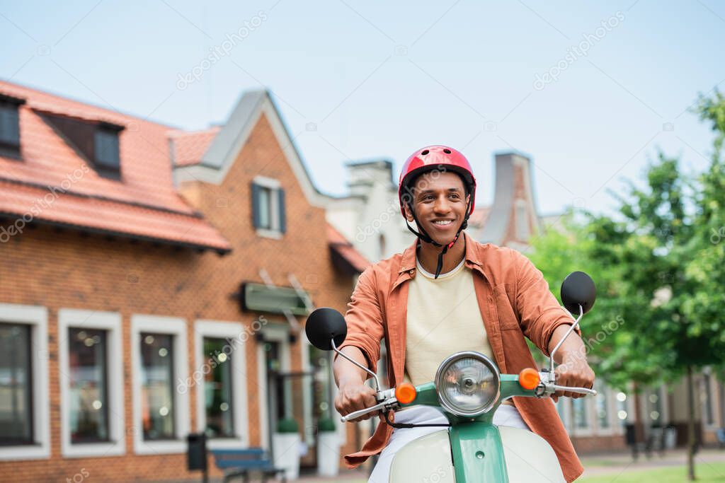 smiling african american man in helmet riding scooter in city