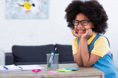 Gözlüklü Afro-Amerikan çocuk evdeki kırtasiyenin yakınındaki kameraya bakıyor. 
