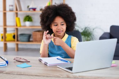 Afro-Amerikalı kız laptopun yanında parmaklarını ve masadaki kırtasiyeyi sayıyor. 