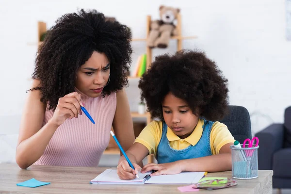 Enojado Africano Americano Madre Apuntando Con Pluma Cerca Hija Escritura —  Fotos de Stock